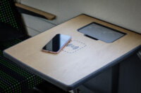 Auf dem Bild sehen Sie einen Tisch im Siemens Mireo, in den eine induktive Ladestation eingebaut ist. Damit können Sie ihr Smartphone aufladen. Auf dem Bild liegt ein Smartphone neben der Ladestation.