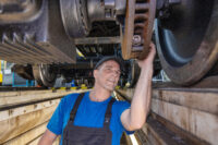 Auf diesem Bild sehen Sie einen Mitarbeiter, der in der Werkstatt unter dem Zug arbeitet.