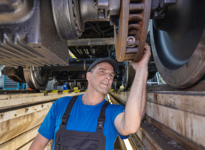 Auf diesem Bild sehen Sie einen Mitarbeiter, der in der Werkstatt unter dem Zug arbeitet.