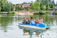 Familie mit Kindern die auf dem Hammersee in Bodenwöhr mit einem Tretboot fahren. Im Hintergrund ist der Badeplatz mit Matschbereich zu sehen.