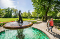 Spaziergänger am Tritonbrunnen im sommerlichen Max Reger Park