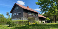 Das Marktredwitzer Haus ist im Sonnenschein seitlich zu sehen. Im Vordergrund ist alles voller grüner Hecken, Wiese und Bäume. Der Himmel ist blau.