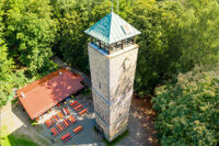 Die Fotoaufnahme zeigt von oben betrachtet den Vierlingsturm und die Strobelhuette auf dem Fischerberg. Rings herum ist grüner Wald im Sonnenschein zu sehen.