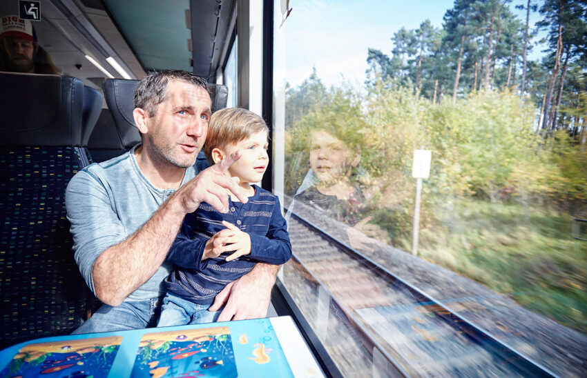 Auf dem Bild sieht man einen Mann mit seinem Kind. Beide schauen aus dem Fenster der oberpfalzbahn.