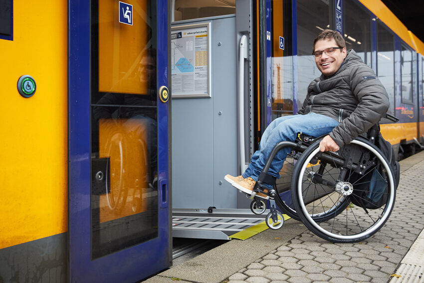 Auf dem Bild sieht man einen Mann im Rollstuhl, der mithilfe einer Rampe in die oberpfalzbahn einsteigen kann.