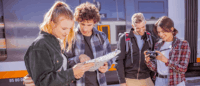 Eine Gruppe von Personen schaut in eine Wanderkarte und in eine Kamera am Bahnhof.