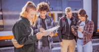 Eine Gruppe von Personen schaut in eine Wanderkarte und in eine Kamera am Bahnhof.