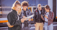 Eine Gruppe von Personen schaut in eine Wanderkarte und in eine Kamera am Bahnhof.