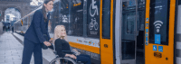 Zugbegleiterin schiebt eine Person im Rollstuhl in den Zug.