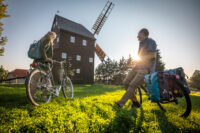 Zwei Radfahrer machen halt auf dem Zwillingsradweg bei Oderwitz. Im Hintergrund sieht man eine Windmühle und den Sonnenuntergang.