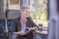 Ein Fahrgast sitzt gemütlich im trilex, trinkt einen Coffee-to-go und liest unser Länderbahn-Kundenmagazin.