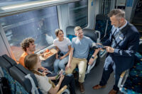 Eine Gruppe Jugendlicher sitzt in einem Vierer im trilex und kauft ihre Fahrkarte beim Kundenbetreuer im Zug.