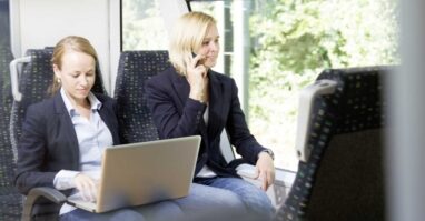 Zwei Pendler fahren mit der Vogtlandbahn, eine Person tippt etwas auf dem Laptop die andere Person telefoniert