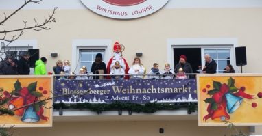 Blossersberger Christkindlmarkt Der Nikolaus steht mit Engel und Krampus am Balkon vom Blossersberger Keller, links und rechts stehen noch ein paar Leute