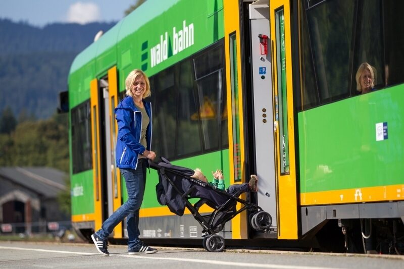 Mutter die mit dem Kinderwagen in die Waldbahn einsteigt