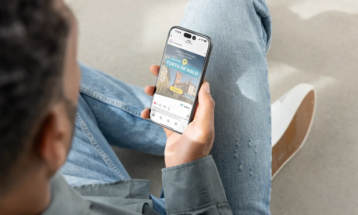 Person hält ein Smartphone in der Hand und betrachtet eine Citytour-Anzeige für Furth im Wald auf dem Bildschirm.