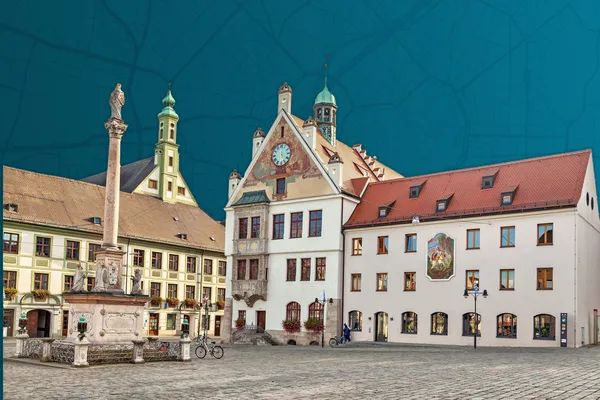 Platz mit barocken Gebäuden, Uhrturm und Mariensäule unter blauem Himmel.