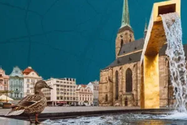 Das Bild zeigt einen goldenen Brunnen mit Wasserfall auf dem Marktplatz von Pilsen. Im Hintergrund steht eine große Kirche mit hohem Turm, umgeben von historischen Gebäuden.