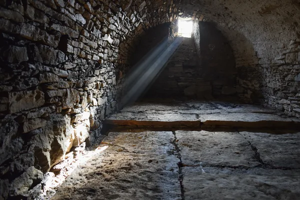 Steinraum mit gewölbter Decke und Lichtstrahlen, die durch ein kleines Fenster fallen.