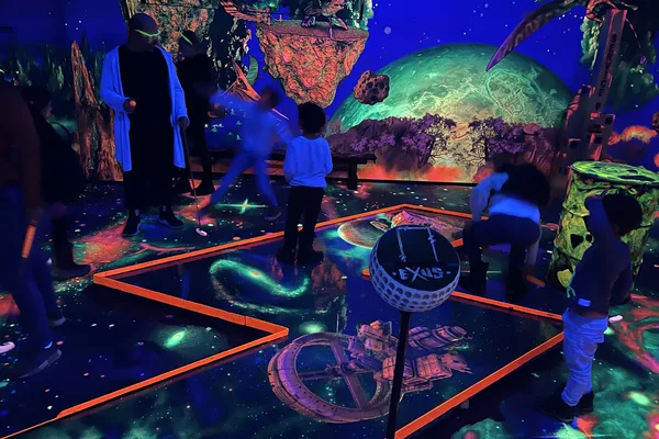 Innenraum mit leuchtenden Minigolfbahnen und bunten Neon-Elementen im Schwarzlicht.