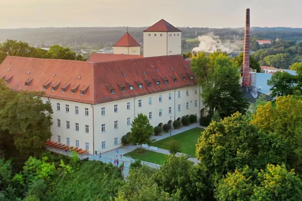 Luftaufnahme der Weihenstephan Brauerei mit rotem Dach, Schornstein und grüner Umgebung.