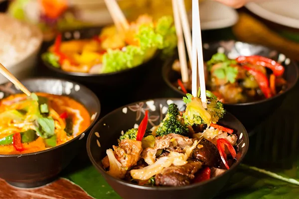 Nahaufnahme von Schalen mit asiatischen Gerichten, frischem Gemüse und bunten Zutaten.