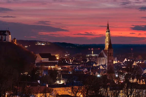 Panorama von Landshut mit Martinskirche und Burg Trausnitz im Abendlicht, rote und violette Himmelsfarben.
