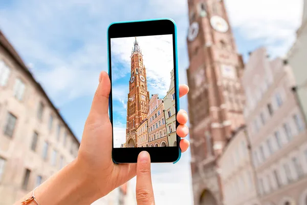 Hand hält Smartphone mit Foto der Martinskirche, im Hintergrund die echte Kirche und historische Häuser.
