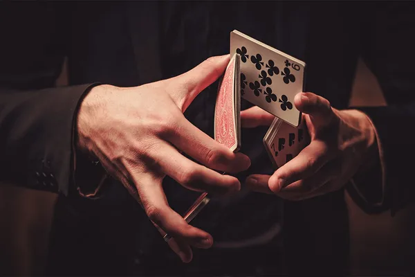 Nahaufnahme von Händen, die Spielkarten kunstvoll mischen, warme Lichtstimmung, Show-Atmosphäre.