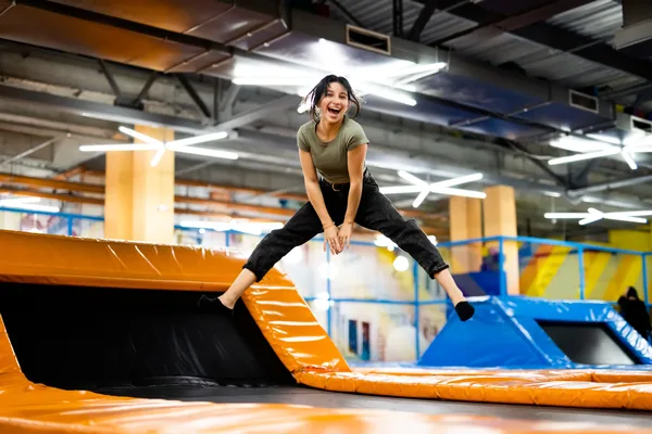 Person springt in einem Indoor-Trampolinpark mit orangefarbenen Sprungflächen und blauen Sicherheitsnetzen.