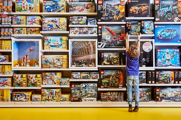 Kind steht vor einem Regal voller LEGO-Sets, darunter Technic- und City-Modelle.