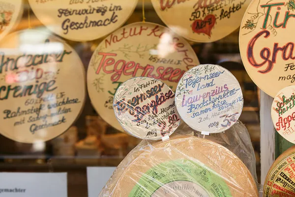 Schaufenster mit handbeschrifteten Schildern und verschiedenen Käsesorten, darunter Tegernseer Bergkäse.