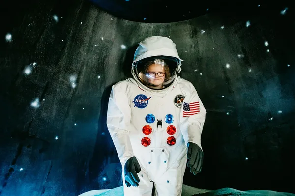 Astronautenanzug mit NASA-Logo in einer Raumfahrt-Ausstellung vor dunklem Hintergrund mit Sternen.