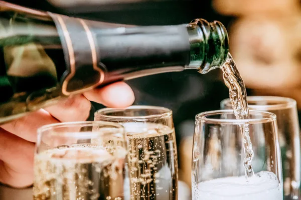Nahaufnahme einer Hand, die Sekt in Gläser einschenkt, mit sprudelnden Blasen.