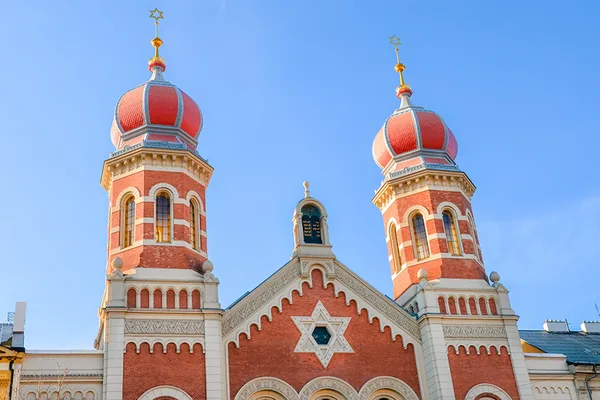 Frontansicht der Großen Synagoge mit roten Zwiebeltürmen und goldenen Sternen unter blauem Himmel.