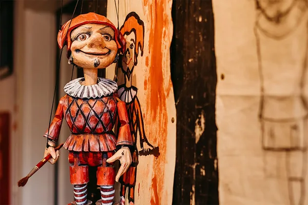 Holzmarionette in rotem Kostüm vor bemaltem Hintergrund, Teil einer Theaterausstellung.