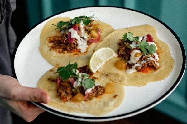 Drei Tacos auf einem Teller, garniert mit Fleisch, Gemüse, Kräutern und Limettenscheibe.