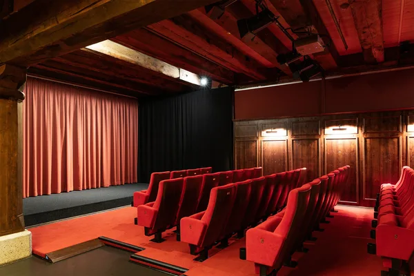Kleiner Kinosaal mit roten Sesseln, Holzdecke und geschlossener roter Bühne.