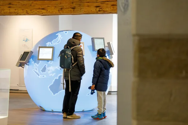 Große blaue Weltkugel mit Bildschirmen und zwei Personen, die die Ausstellung erkunden.