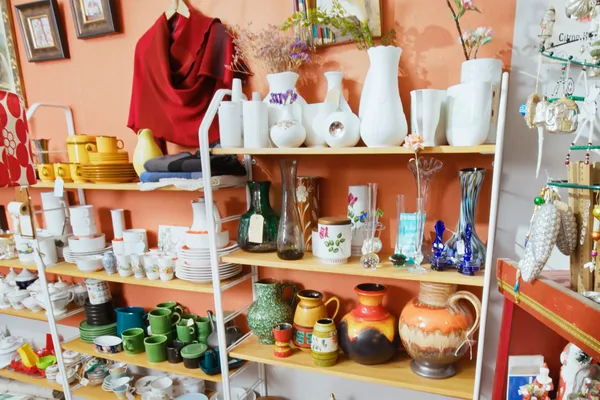 Regale mit buntem Geschirr, Vasen und Dekorationsartikeln in einem Second-Hand-Laden.