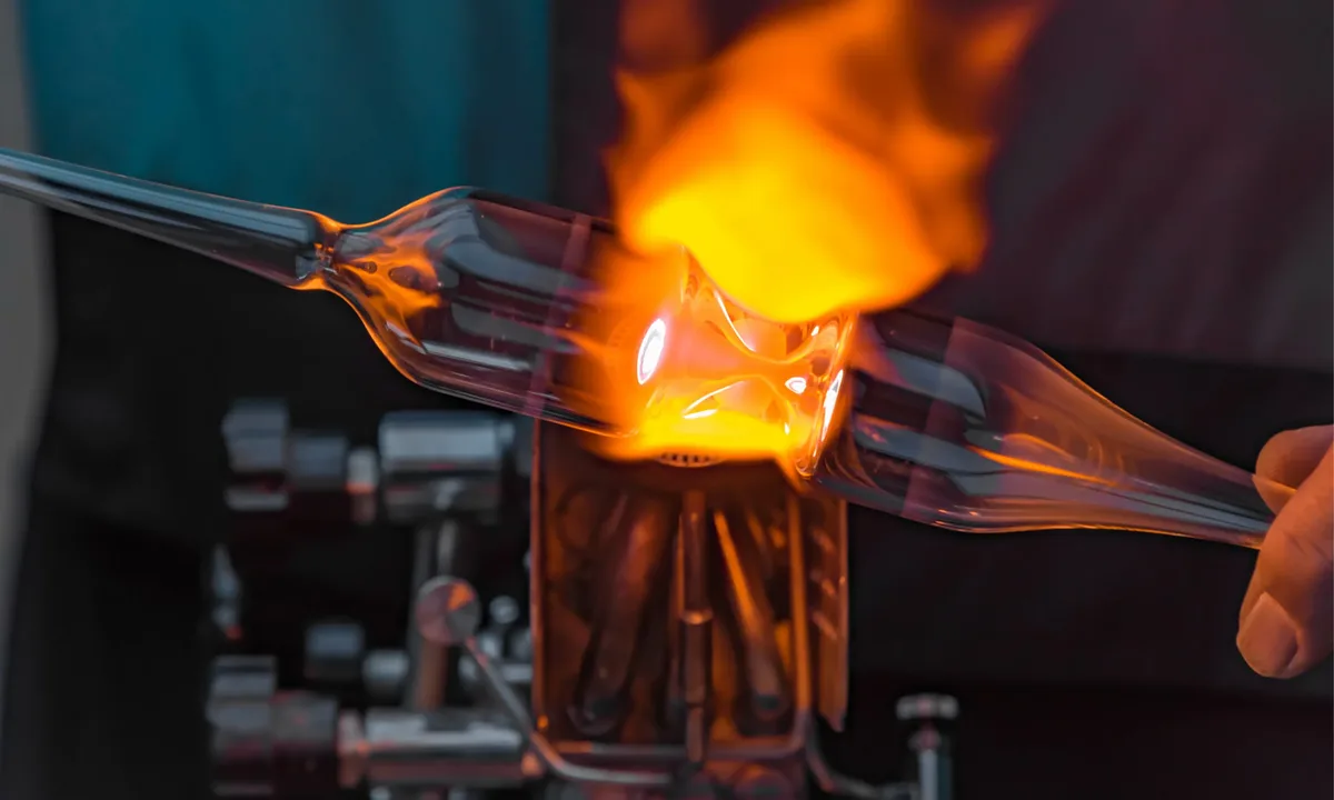 Nahaufnahme einer Glasbläserarbeit mit glühendem Glas und Flamme.
