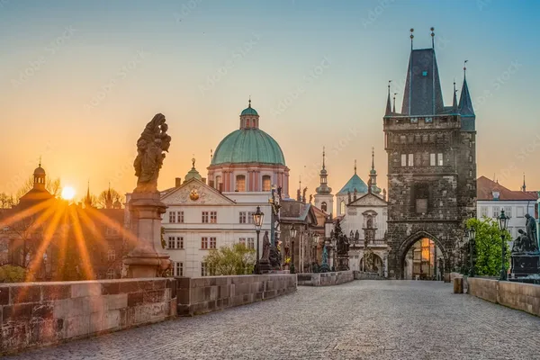 Historische Karlsbrücke mit Kopfsteinpflaster, barocken Statuen und Blick auf den Altstädter Turm bei Sonnenaufgang.