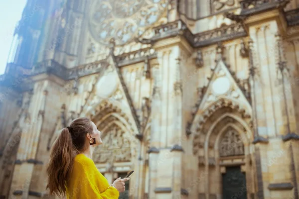 Person betrachtet die kunstvolle Fassade des Veitsdoms in Prag und hält ein Smartphone.