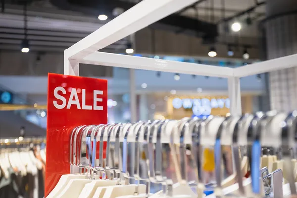 Kleiderstange mit weißen Bügeln und rotem SALE-Schild in einem modernen Outlet.