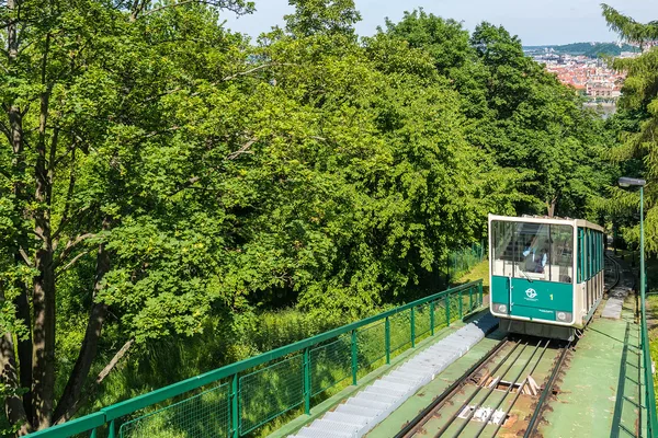 Grüne Seilbahn fährt durch bewaldetes Gebiet mit Blick auf die Stadt Prag im Hintergrund.