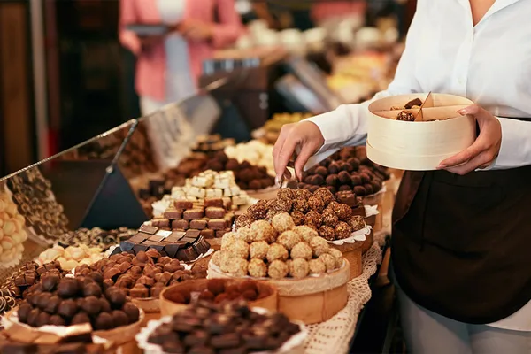 Person wählt Pralinen aus einer großen Auswahl an Schokoladenspezialitäten.