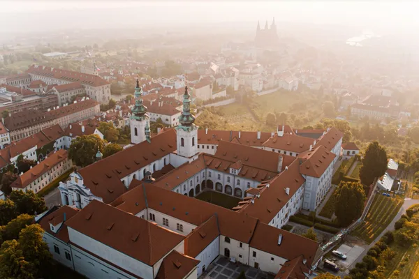 Luftaufnahme des Strahov-Klosters mit roten Dächern und Blick auf die Prager Burg im Hintergrund.