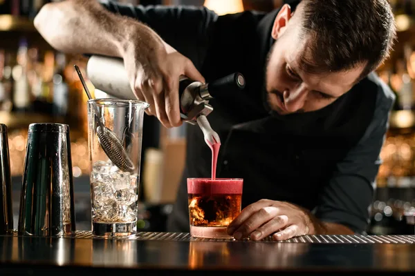 Bartender bereitet einen Cocktail an einer stilvollen Bar mit glänzenden Shakern und Gläsern.