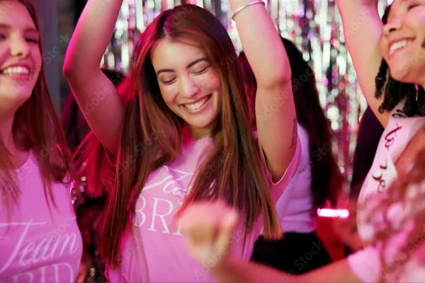 Menschen tanzen in einem Club unter bunten Lichtern und feiern ausgelassen.