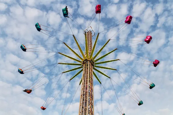 Hohes Kettenkarussell mit bunten Sitzen vor blauem Himmel mit Wolken.